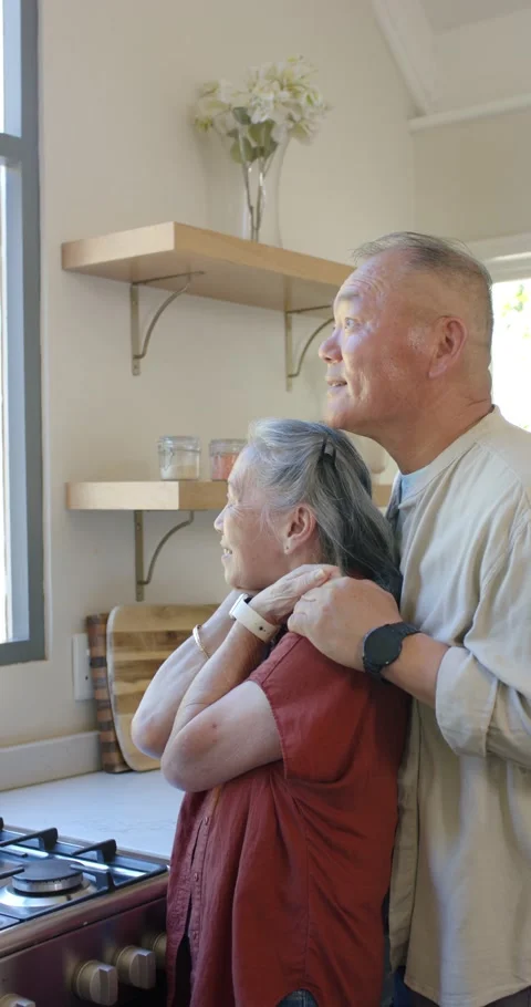Vertical video: Asian couple, man holding her shoulders at kitchen counter, Stockbeeldmateriaal 345322053
