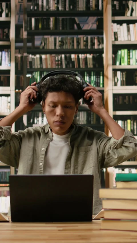 Vertical Video Asian student using headphones and taking notes with laptop and Stock Footage 337530098