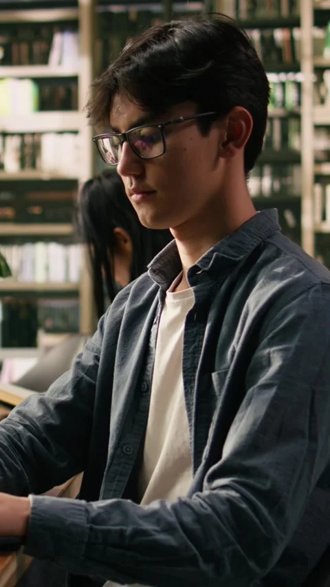 Vertical Video Asian student working on laptop in quiet library with tall Stock Footage 336379616