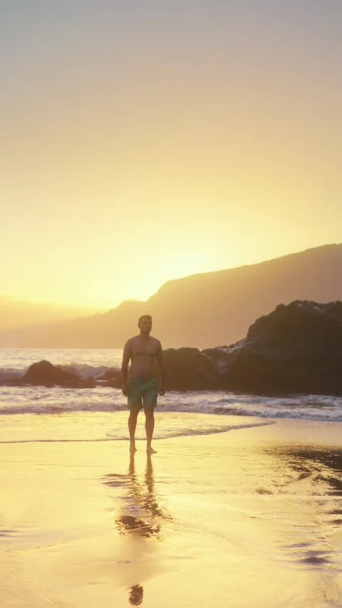 Vertical video of attractive man walking on black beach at sunrise Video stock 299960425