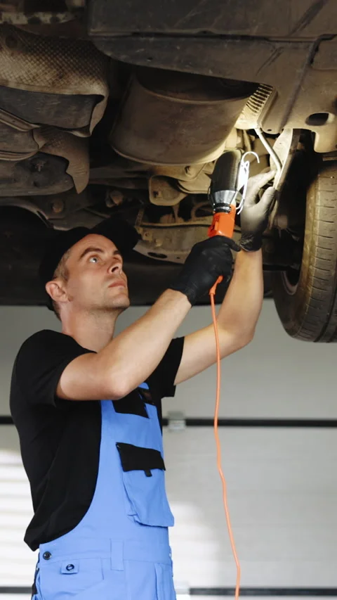 Vertical Video of Auto mechanic man in blue overalls with lamp working at Stock Footage 305176251