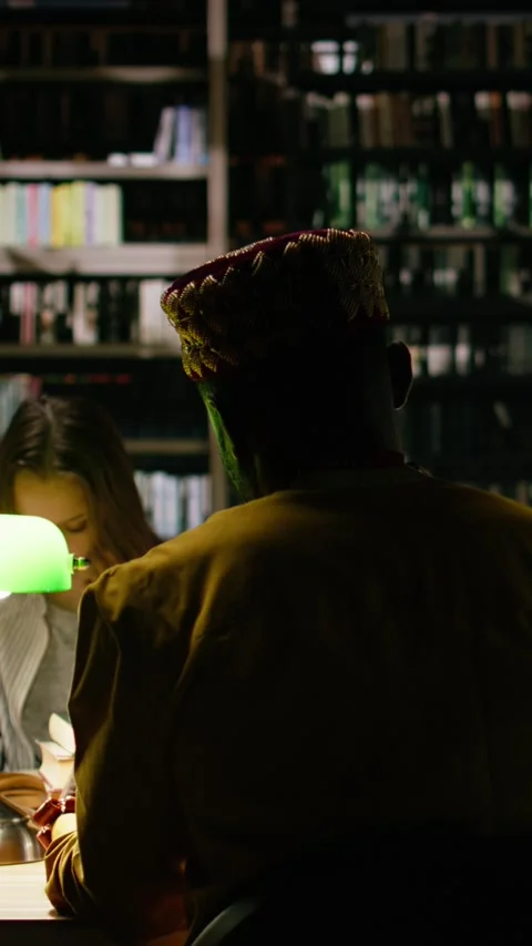 Vertical Video Back view of adult learner in traditional clothes at dark library Stock Footage 337530008