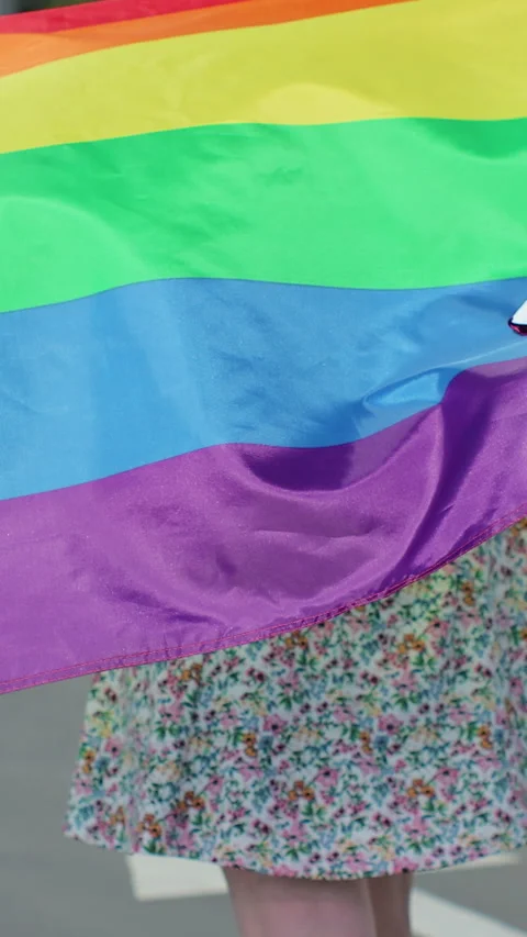 Vertical video. Back view of young Woman holding LGBT rainbow flag while walking 库存影片 348289148