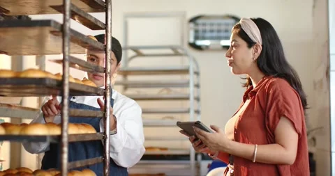 Vertical video: Baker in chef coat inspecting rolls on rack in bakery, colleague Stock Footage 342233995