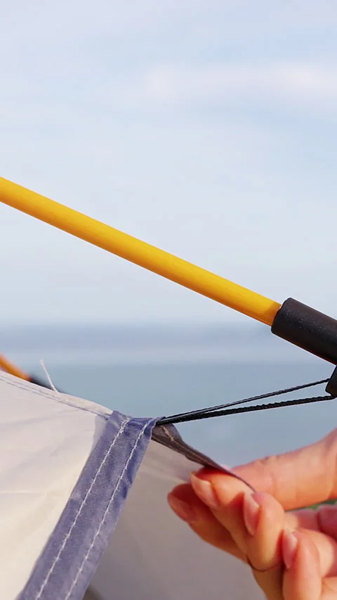 Vertical video. Bare Hands Secure a Yellow Pole to a Beige Camping Tent, Close V Stock Footage 348753105