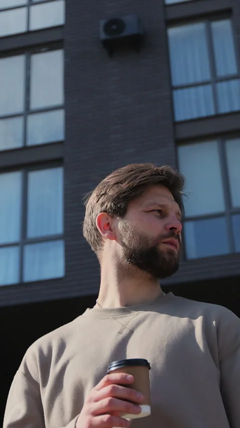 Vertical video. Bearded man with coffee, looking into camera on the street. Stock-Footage 344109034