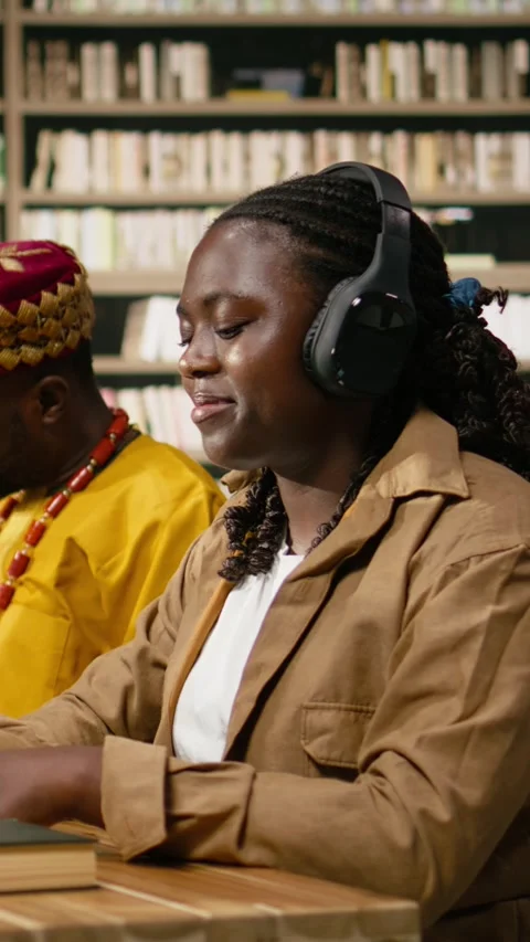 Vertical Video Black student wearing headphones reading open book at desktop Stock Footage 337529021