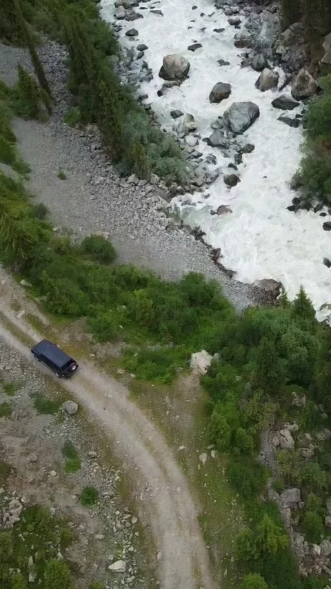 Vertical video: Black SUV Driving by Rushing Mountain River Diagonal Stock Footage 331991907