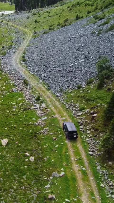 Vertical video: Black SUV Driving by Massive Mountain Rock Field Aerial Stock Footage 332010701