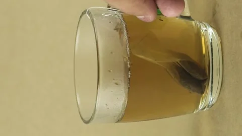 Vertical video black tea bag lifting and dropping into glass transparent mug to Stock Footage 151999792
