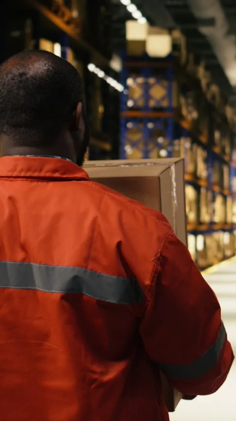 Vertical Video Black worker moving cargo pallets across busy warehouse floor Stock Footage 333090628