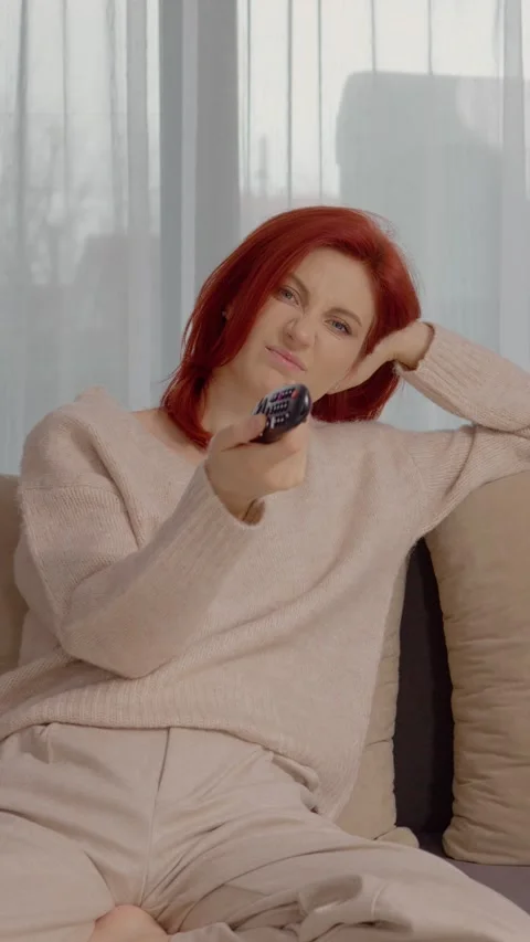 Vertical video Bored woman changes TV channels on the couch in empty room 스톡 동영상 334020693