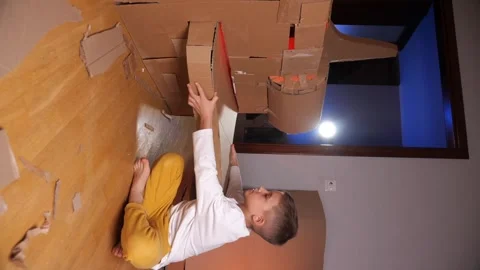 Vertical video A boy builds a plane out of cardboard. Pilot and airplane game Video stock 256498259