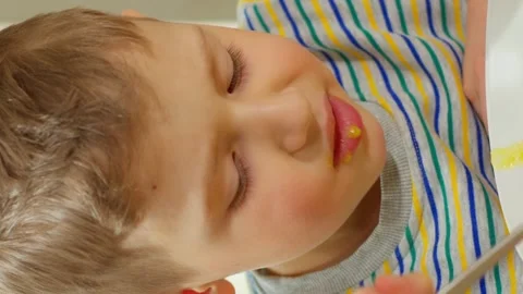 Vertical video. The boy smiled into the camera and began to eat a spoonful of Stock-Footage 250454404