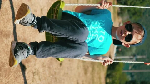Vertical video. boy in sunglasses swing on a swing Stock Footage 148261777