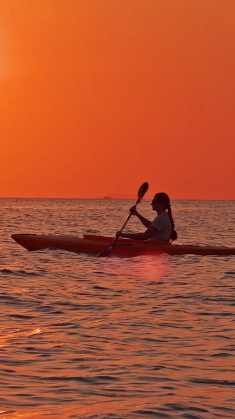 Vertical video. A bright orange sunset over the open sea with a single kayak in Stock Footage 329640816
