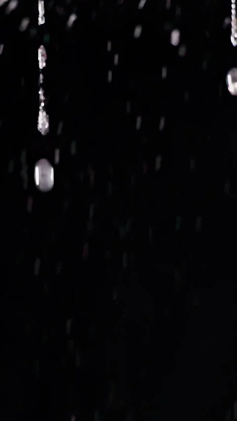 Vertical video. Bright Rain Droplets Fall Through Darkness Against a Deep Black Stock Footage 341423089