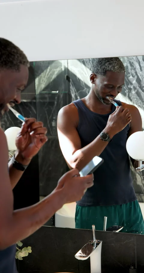 Vertical video: Brushing teeth and checking smartphone, man multitasking in Stock Footage 310540877