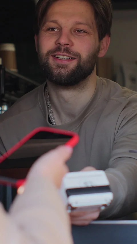 Vertical video. In the cafe man makes takeaway coffee for a customer which pay 動画素材 344107705