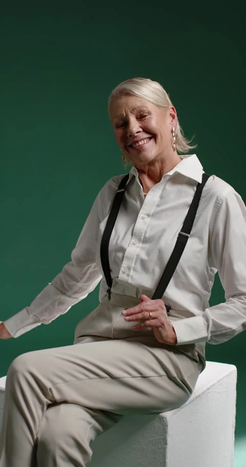 Vertical video: Camera rolling, senior female posing on white cube in studio, Stock Footage 345093471