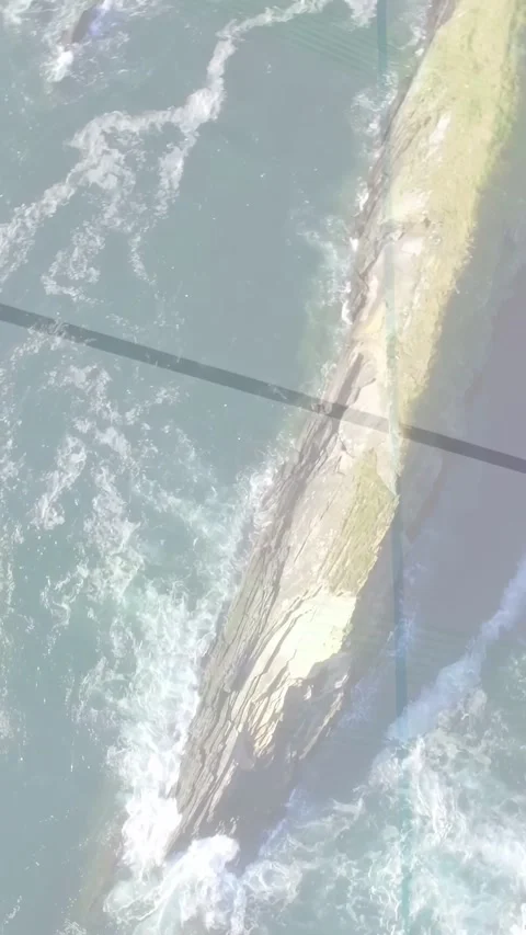 Vertical video: Camera tilting, waves foaming around long spit, grid shadow Stock Footage 333912875