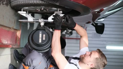 Vertical video. A car mechanic in a workshop attaches a jack to a car. Stock Footage 212345149