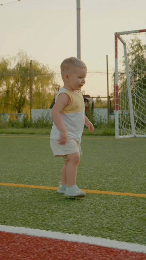 Vertical video Cheerful boy plays with a ball on a sunlit sports field during Stock Footage 327584942