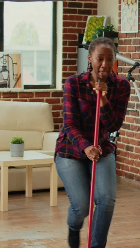 Vertical video: Cheerful girlfriend dancing in apartment and using mop to sweep Vídeos de archivo 229456480