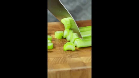 Vertical video. Chef with kitchen knife slices celery stalks on wooden board. Stock Footage 302636120