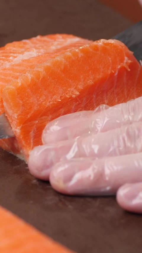 Vertical video. The chef's gloved hand cuts salmon meat into thin pieces with a Video stock 300338379