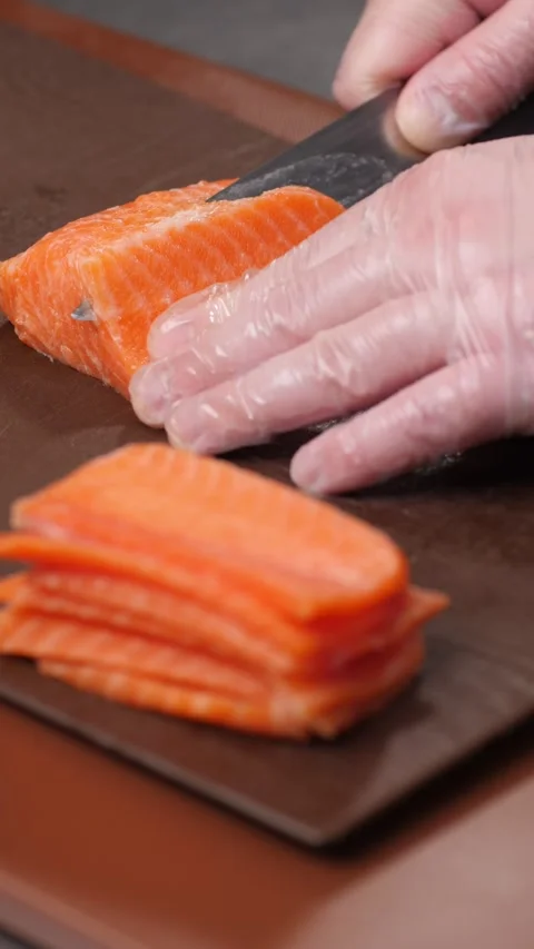 Vertical video. The chef's hand cuts the salmon meat into thin pieces with a Video stock 289082120
