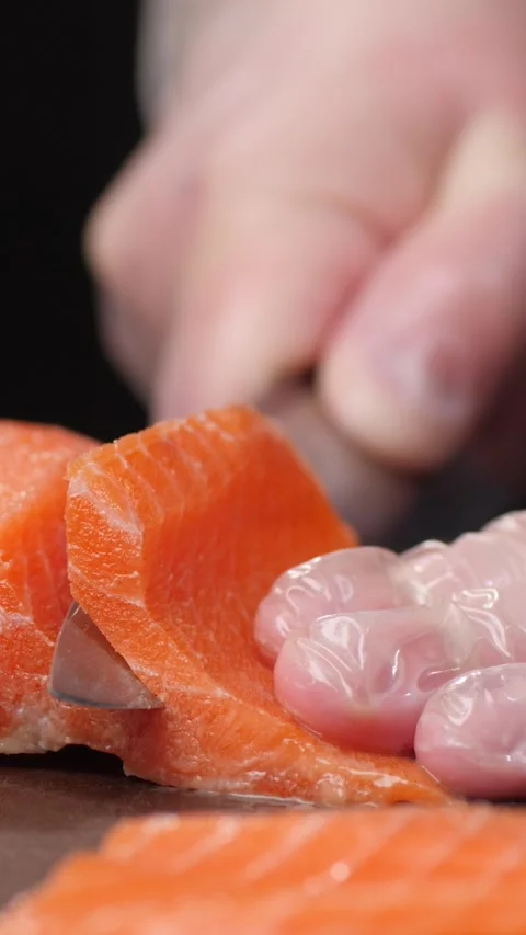 Vertical video. The chef's hand cuts the salmon meat into thin pieces with a Video stock 295188809