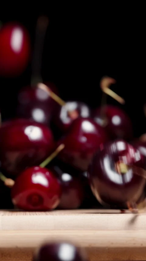 Vertical video. A cherry falls down from a wooden board against a black backgrou Stock Footage 249568531
