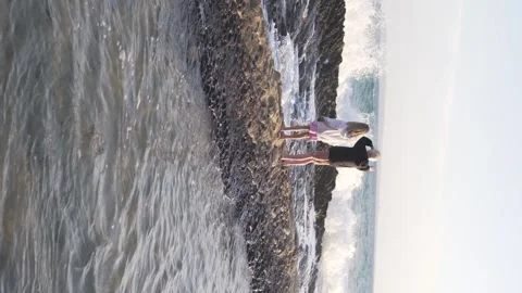 Vertical video, children standing on a rock in the sea next to high waves, waves Stock Footage 273396044