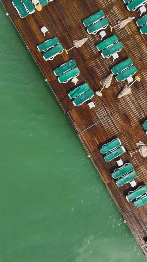 Vertical Video of Clear Blue Waves Moving Under Wooden Pier With Sun Umbrellas Video stock 342306808