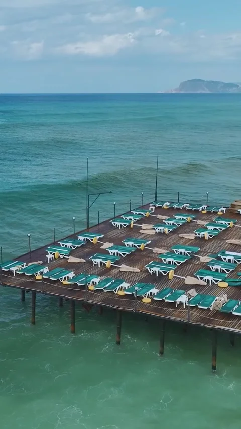 Vertical Video of Clear Water Waves Under Long Wooden Pier With Sun Umbrellas Stock Footage 342305661