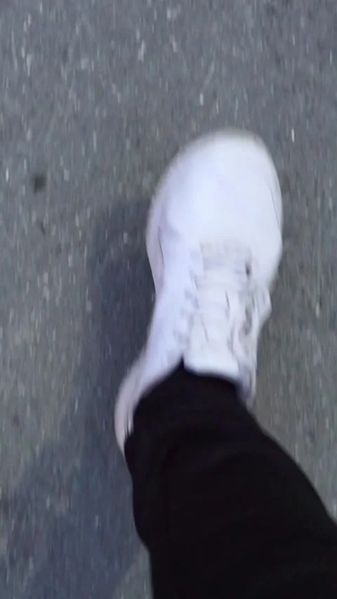 Vertical video close up of feet wearing white sneakers walking on city asphalt Stock Footage 345211838