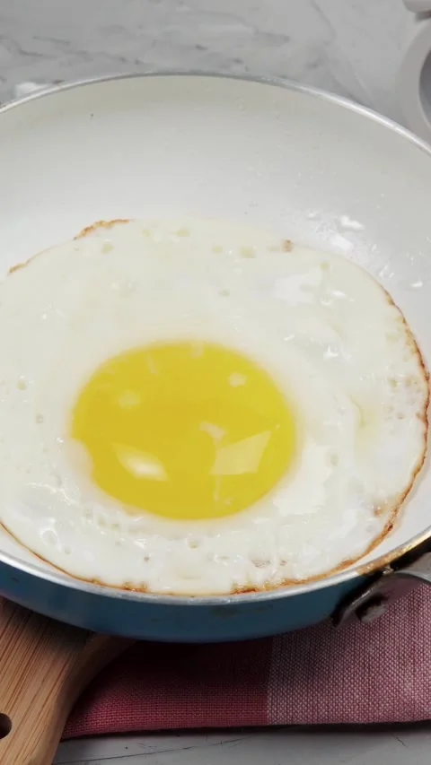 Vertical video close up of frying sunny side up eggs sizzling in hot pan Stock Footage 345212207