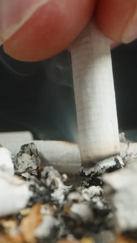 extinguish a cigarette Vertical video. A close-up of a hand extinguishing a cigarette butt in a  pile of