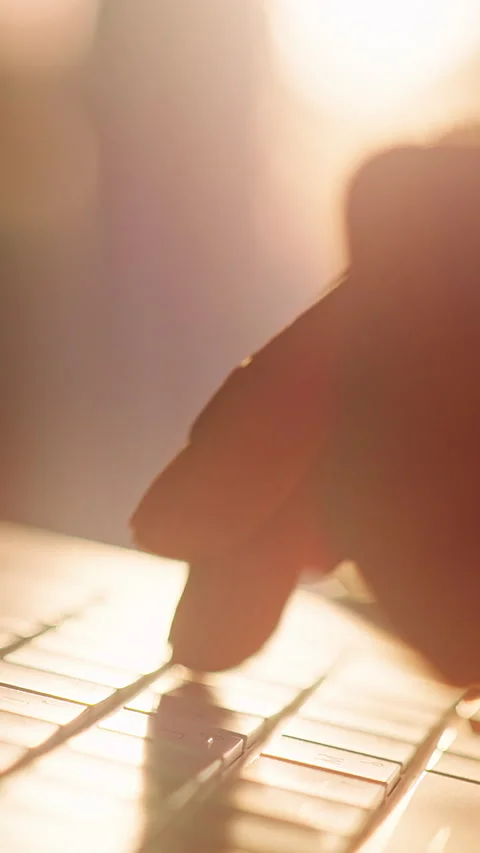 Vertical video. Close Up of Hand Typing on Laptop Keyboard in Warm Sunset Backli Stock Footage 329041988