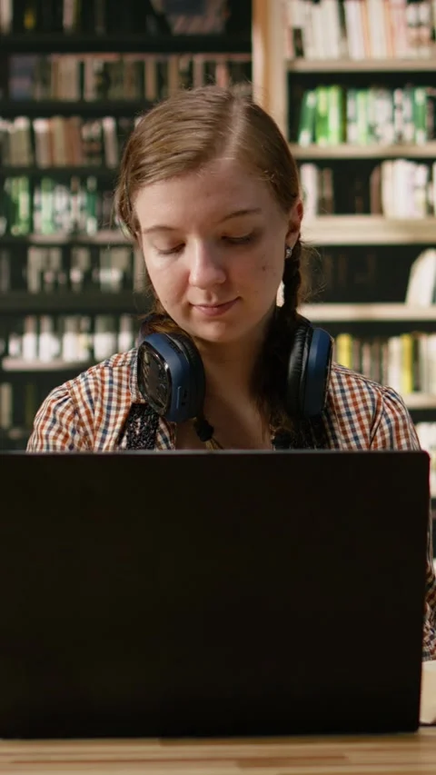 Vertical Video Close-up of hands typing on laptop beside open book on library Stock Footage 337529834