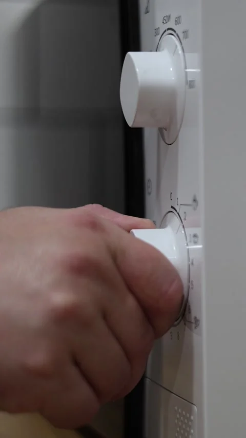 Vertical video close up. Male hand turns knob on white microwave oven Stock Footage 326825678