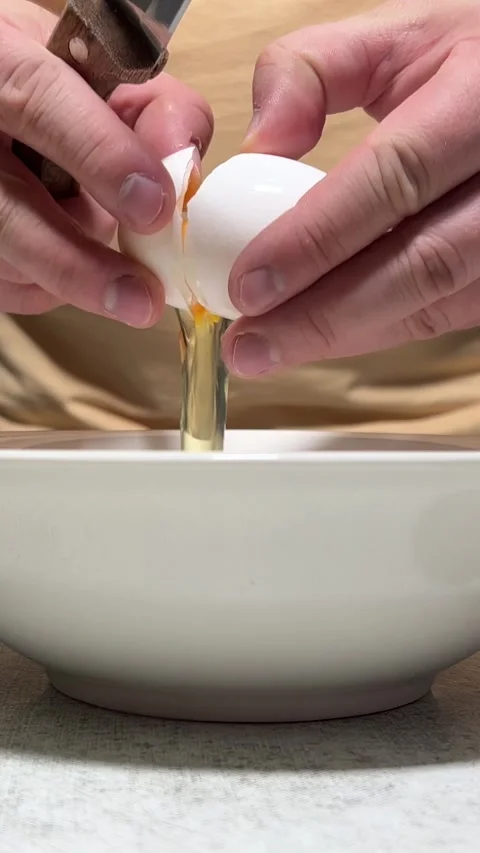Vertical video close up. Man in beige t-shirt with knife breaks chicken egg Stock Footage 289034107