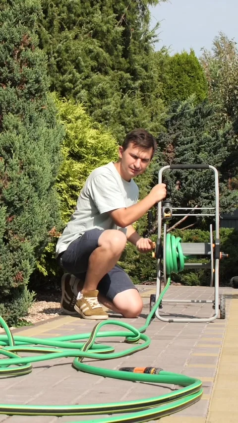 Vertical video close-up man rolls up a garden watering hose into a reel Stock Footage 284725947