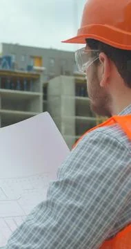 Vertical video. Close-up portrait of engineer with blueprint in front of buil Stock Photos