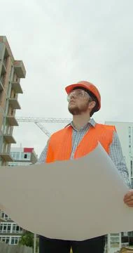 Vertical video. Close-up portrait of engineer with blueprint in front of buil Stock Photos