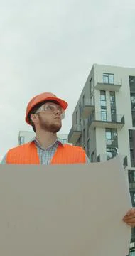 Vertical video. Close-up portrait of engineer with blueprint in front of buil Stock Photos