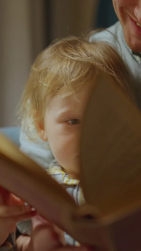 Vertical video: Close up Portrait of Young father sits with a child and reads a Stock Footage 298729844