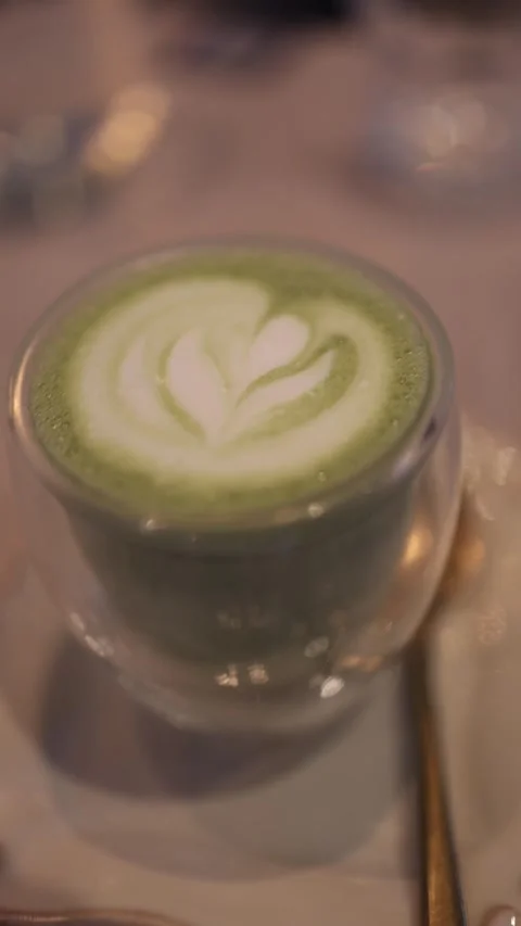 Vertical video: A close-up shot of a matcha latte with intricate latte art on to Stock Footage 300784043