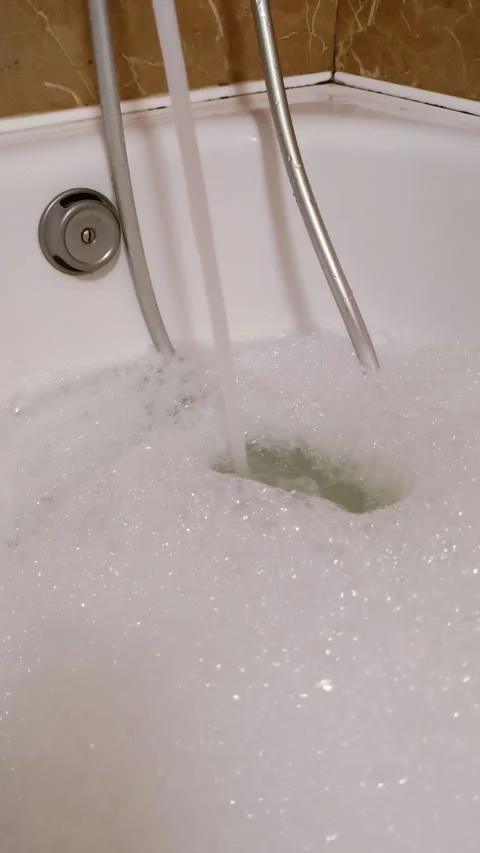 Vertical video close-up of water pouring into bathtub with foam on surface Video stock 313136127